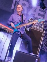 Bilde av mann med langt hår som står på en scene og spiller på en blå elo-bass. foto.