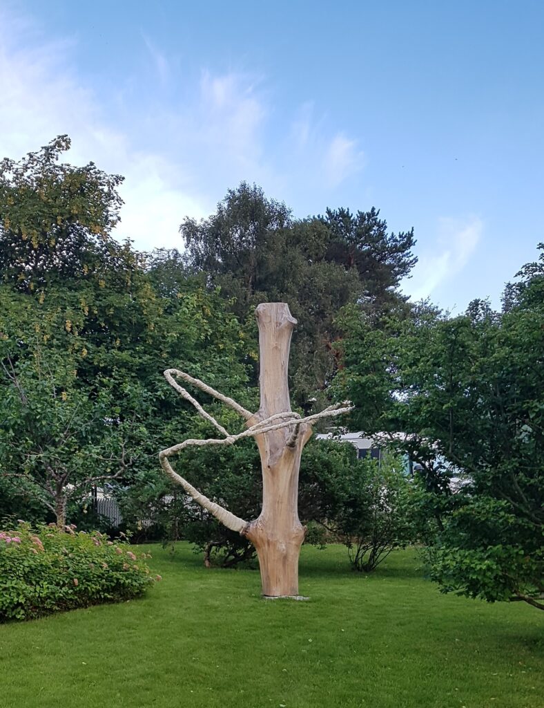 Bilde av skulptur laget av en trestamme med trær i bakgrunnen. foto