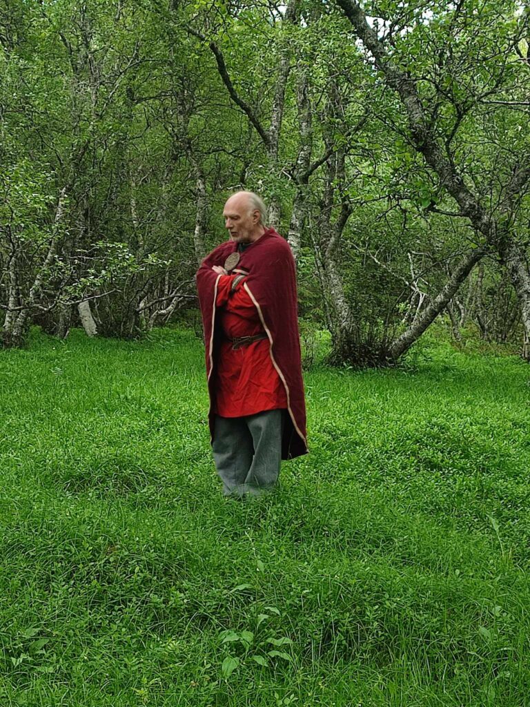 Mann kledd i vikingedrakt står med armene i kors i skogen.foto